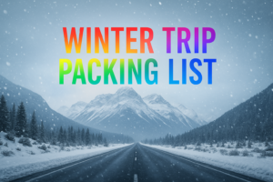 ❄️ Winter Me Ghumne Ke Liye Kya-Kya Zaruri Hota Hai? A vibrant winter travel image featuring a snowy mountain road with snowfall and colorful text reading “Winter Trip Packing List.”